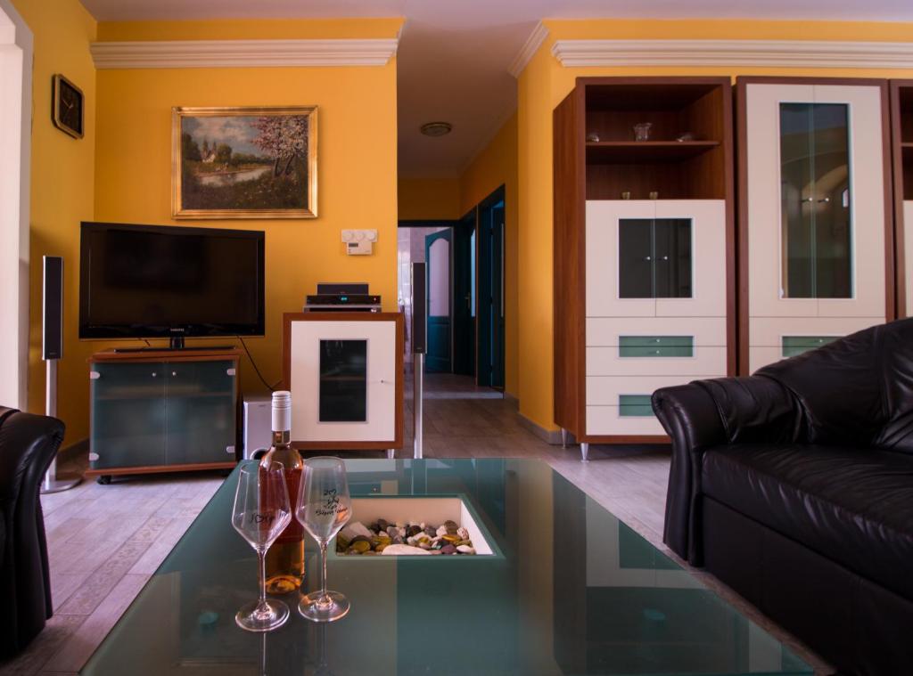 Boros Vendégház Eger في إغير: غرفة معيشة مع طاولة زجاجية مع كأسين من النبيذ