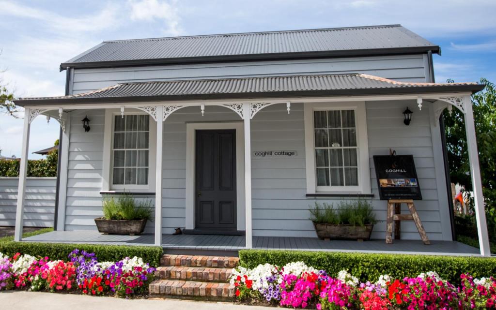 a small white house with flowers in front of it at Coghill Cottage in Whitianga