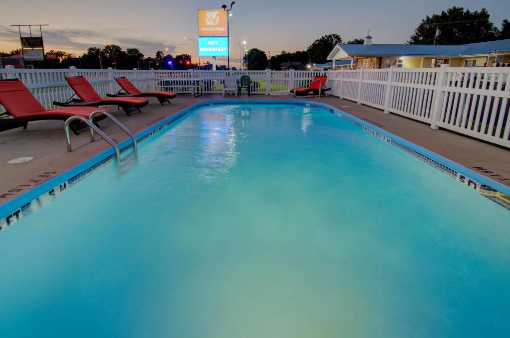 a large swimming pool with red chairs and a fence at Westbridge Inn & Suites in Clinton