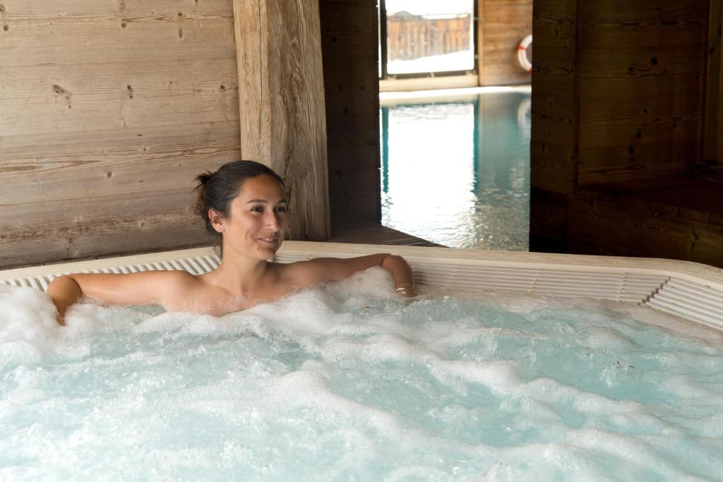 a woman is sitting in a hot tub at Chalet-Hôtel La Marmotte, La Tapiaz & SPA, The Originals Relais in Les Gets