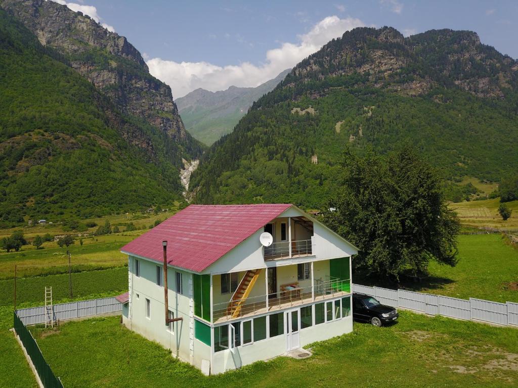 una casa con techo rojo con montañas al fondo en Guest House Gogia en Zhabeshi