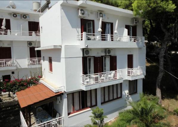 a large white building with balconies and trees at Nikos Rooms in Votsi