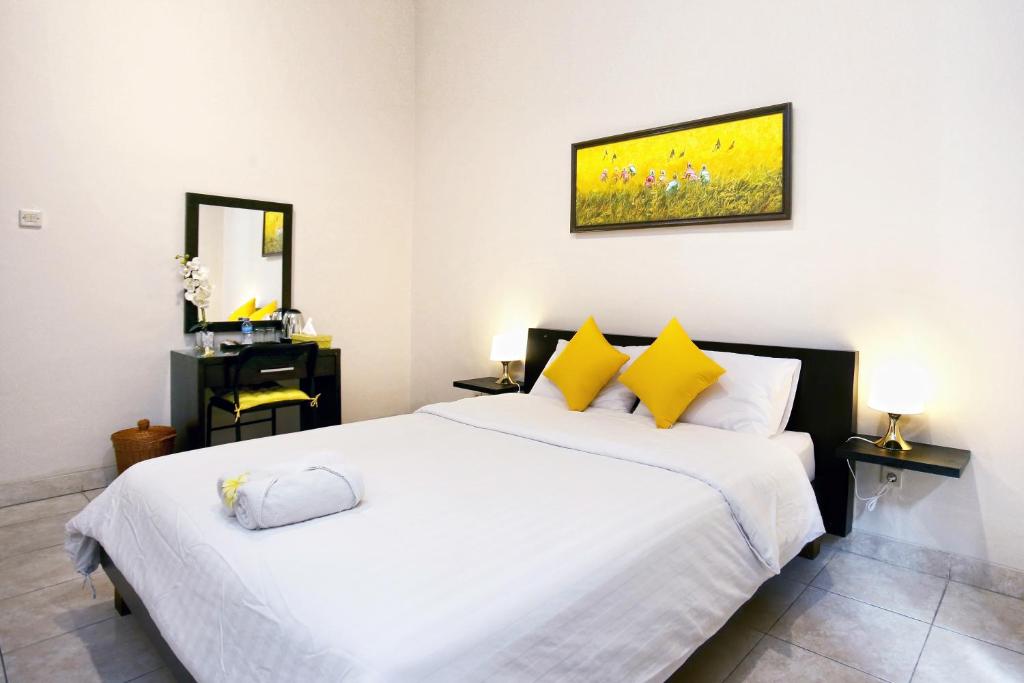 um quarto com uma grande cama branca com almofadas amarelas em Cameng Homestay em Denpasar