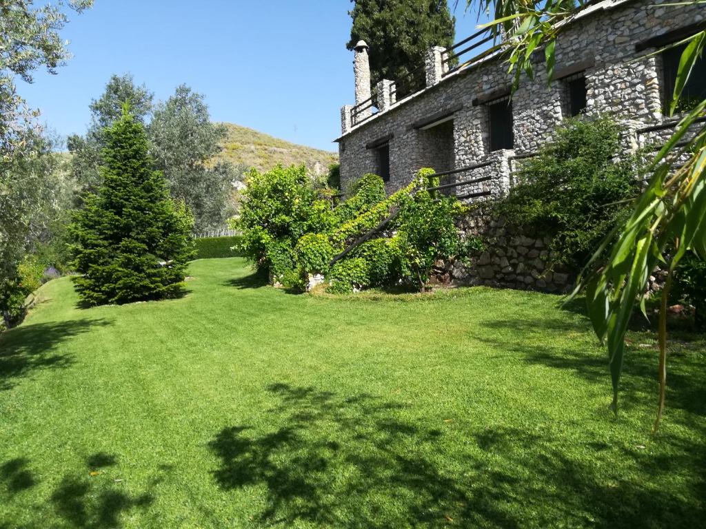 un patio de una antigua casa de piedra con césped verde en Bancal de Los Pérez, en Carataunas