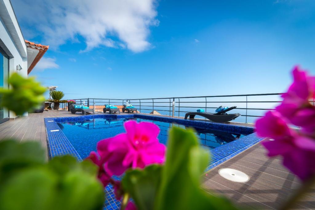 a swimming pool with pink flowers in the foreground at Casa Lira in Arco da Calheta