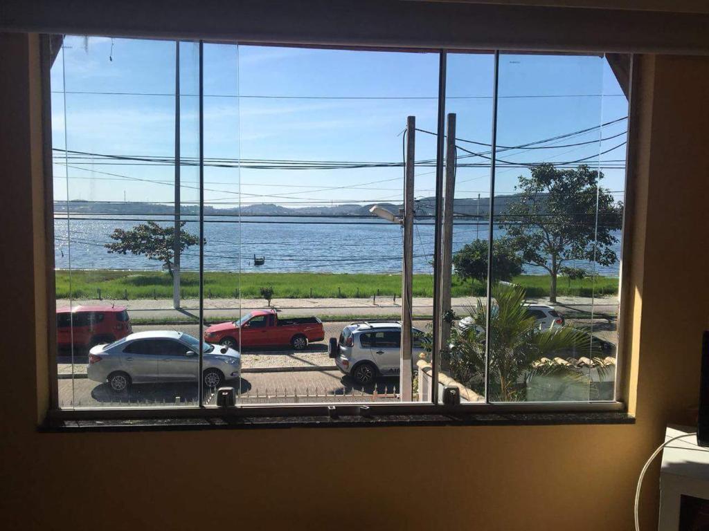 a window with a view of a parking lot and a body of water at Quartos da lagoa in Cabo Frio