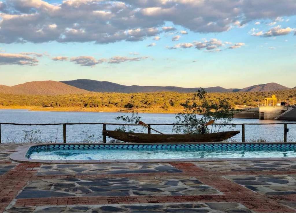 una piscina junto a un cuerpo de agua con un barco en Von Bach Dam Resort, en Okahandja