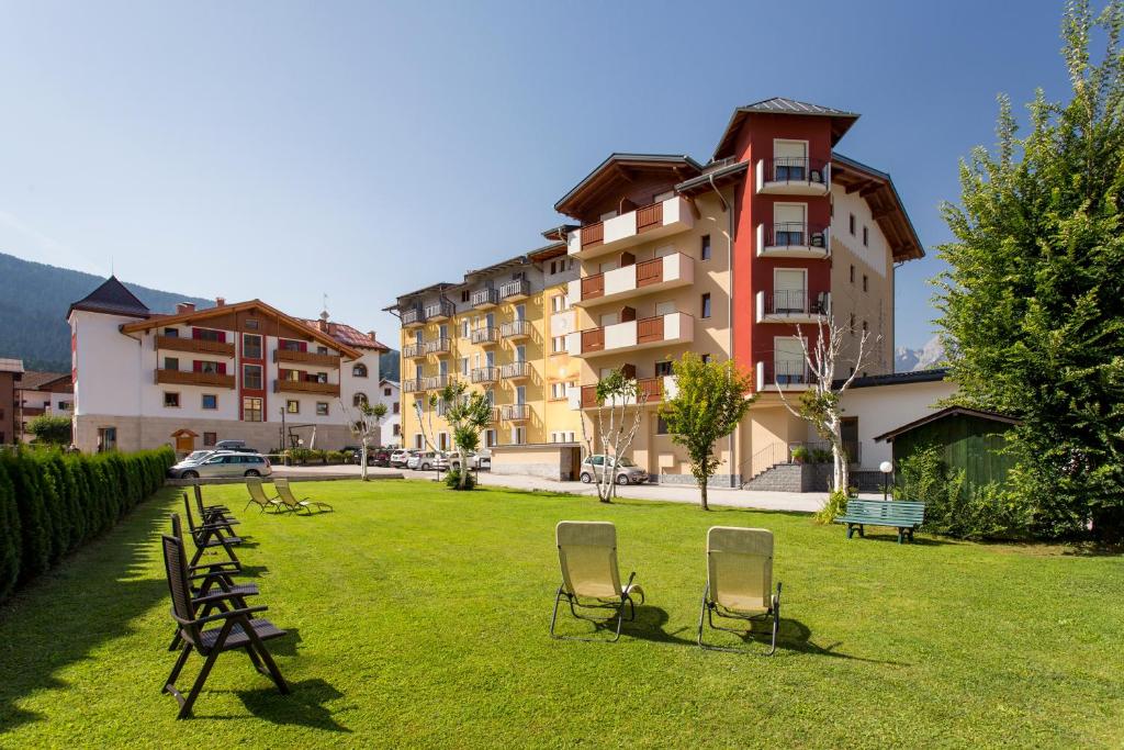 a green yard with chairs and a building at Hotel Stella Alpina in Andalo
