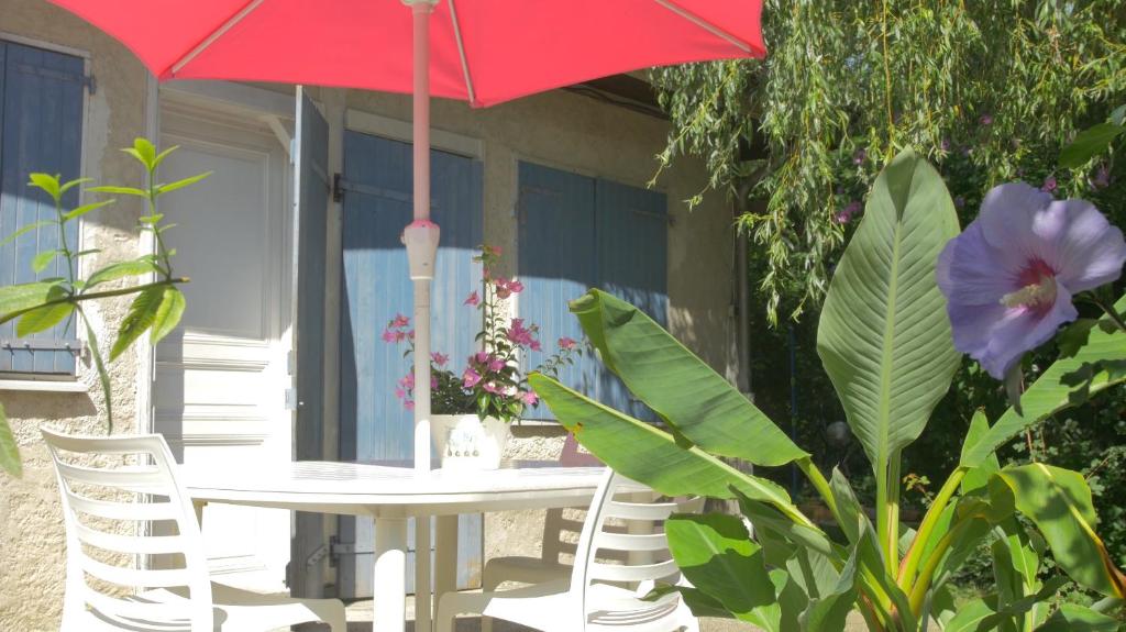 a table and chairs with a red umbrella and flowers at La Ferme de Thoudiere in Saint-Étienne-de-Saint-Geoirs