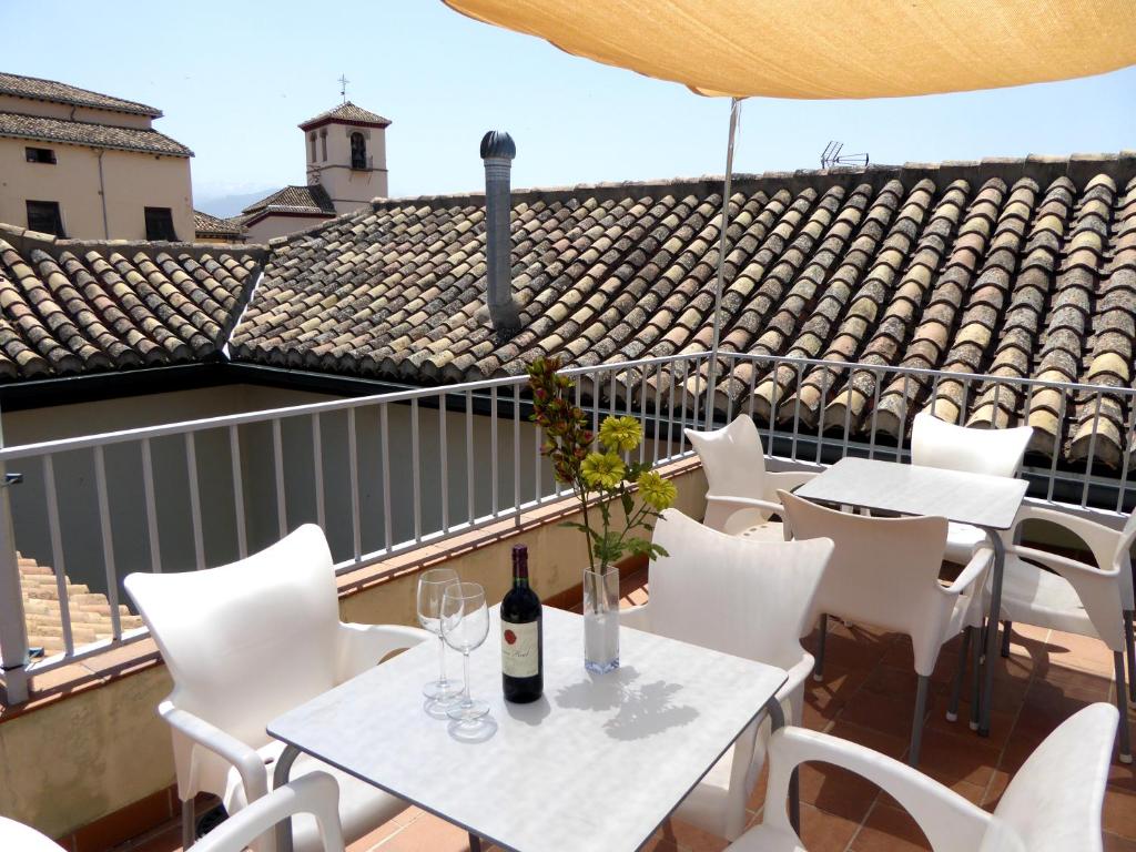 einen Balkon mit weißen Tischen und Stühlen sowie einer Flasche Wein in der Unterkunft Laurel Suites Apartments in Granada