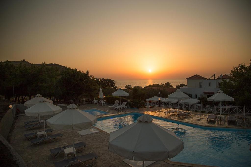 Blick auf einen Pool mit Sonnenschirmen und den Sonnenuntergang in der Unterkunft Akti Hotel & Apartments in Mythimna