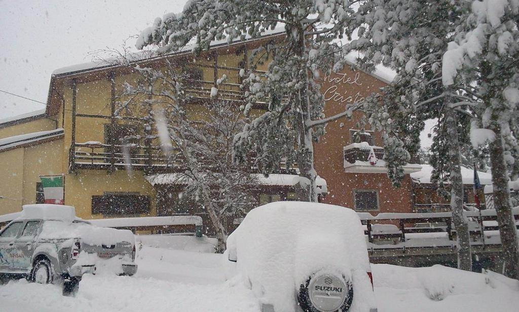 um parque de estacionamento coberto de neve em frente a um edifício em Cristall Hotel em Rocca di Cambio