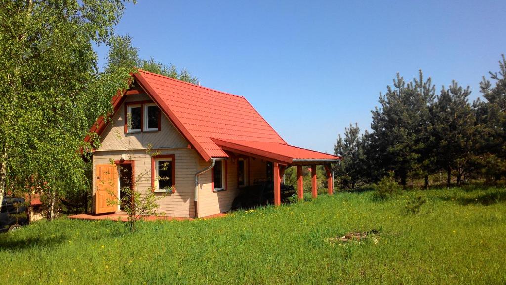 una pequeña casa con techo rojo en un campo en Domek Letniskowy przy lesie, en Kruklanki