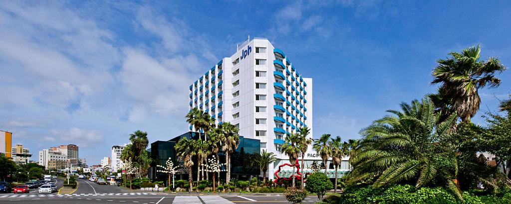 a tall white building with palm trees and a street at Jeju Pacific Hotel in Jeju