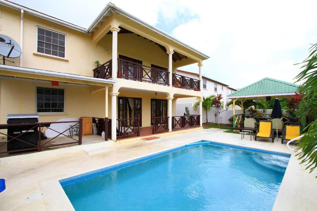 a villa with a swimming pool in front of a house at Sungold House Barbados in Saint Peter