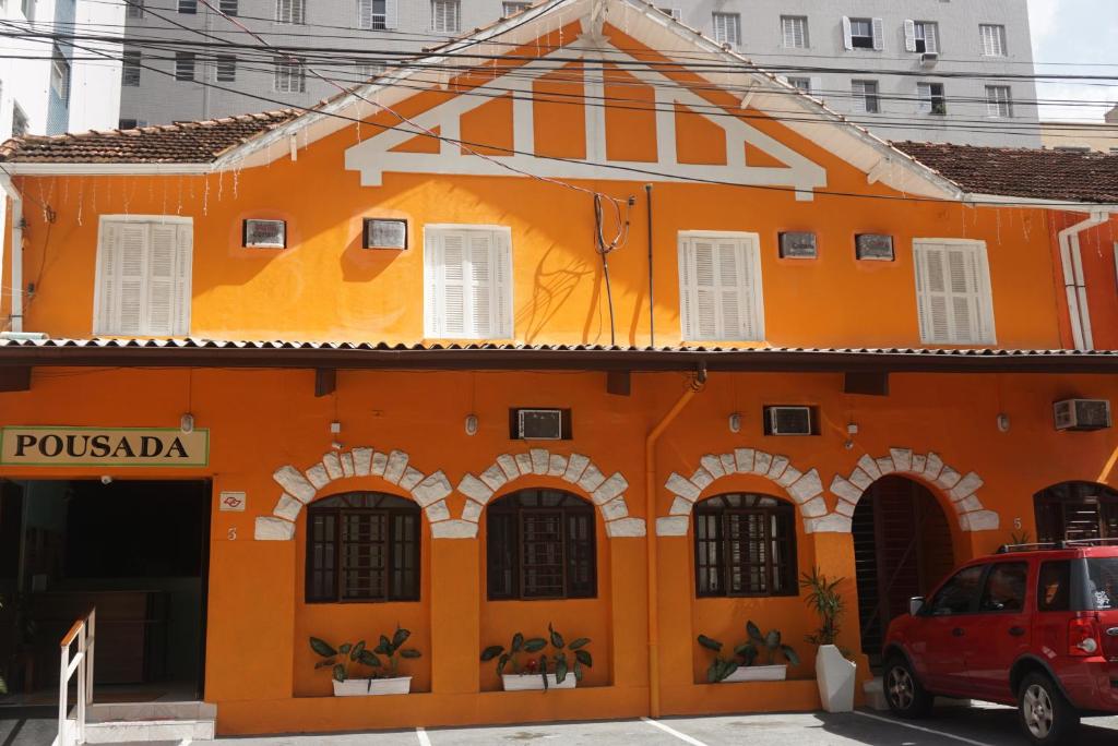 un edificio naranja con un coche rojo aparcado delante en Pousada Orquidário en Santos