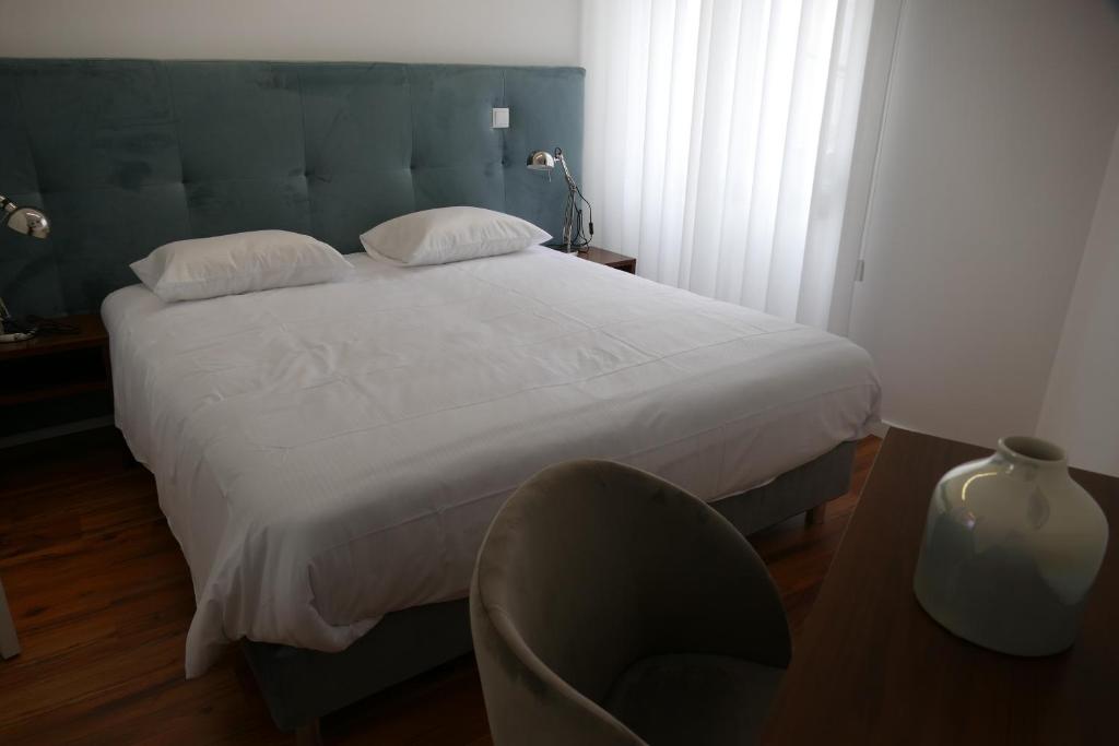 um quarto com uma grande cama branca e uma cadeira em Guest House Eça - Centro Histórico Leiria em Leiria
