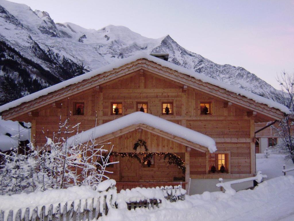 una cabaña de madera cubierta de nieve con montañas al fondo en Chalet Altitude 1057, en Chamonix-Mont-Blanc