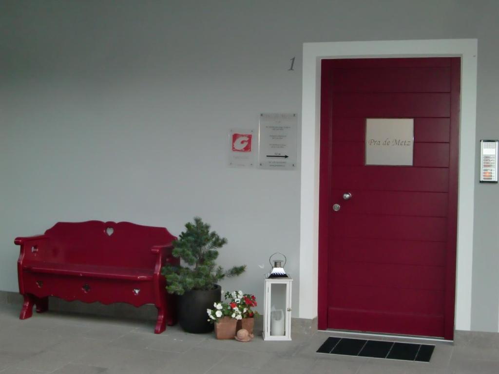 una puerta roja con un banco y una planta al lado en Prà de Metz Apartments en Santa Cristina in Val Gardena