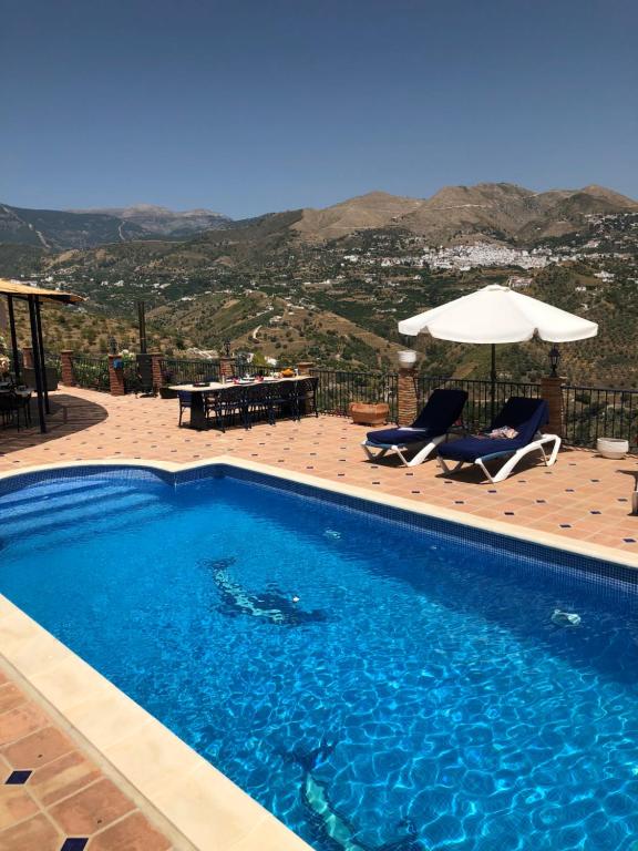 a swimming pool with two chairs and an umbrella at B&B Villa Archez in Árchez