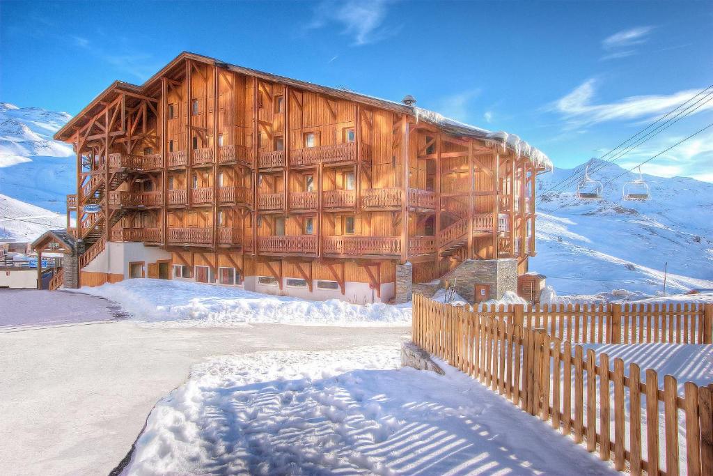een groot houten gebouw in de sneeuw met een hek bij Résidence Les Balcons de Val Chavière in Val Thorens