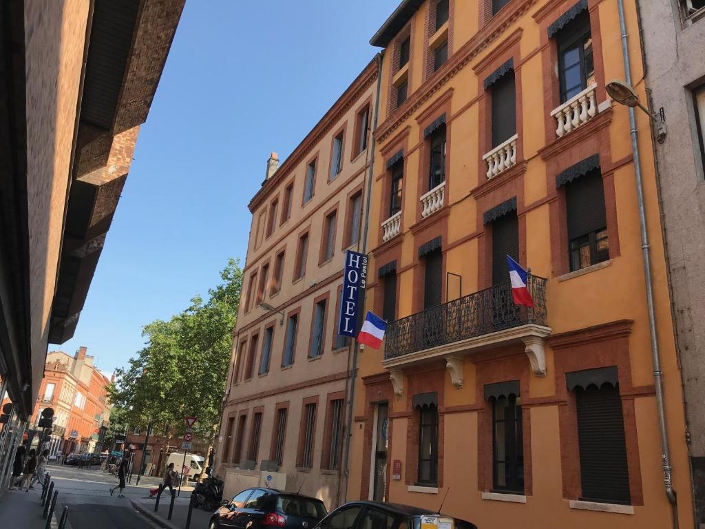 Un edificio in una strada con due bandiere sopra. di Hôtel le Pastel a Tolosa