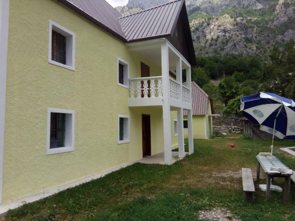 ein gelbes Haus mit Balkon und Sonnenschirm in der Unterkunft Bujtina Ahmetaj in Valbonë