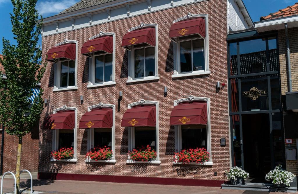 um edifício de tijolos com toldos vermelhos e flores nas janelas em Boutique Hotel Opus One em Numansdorp