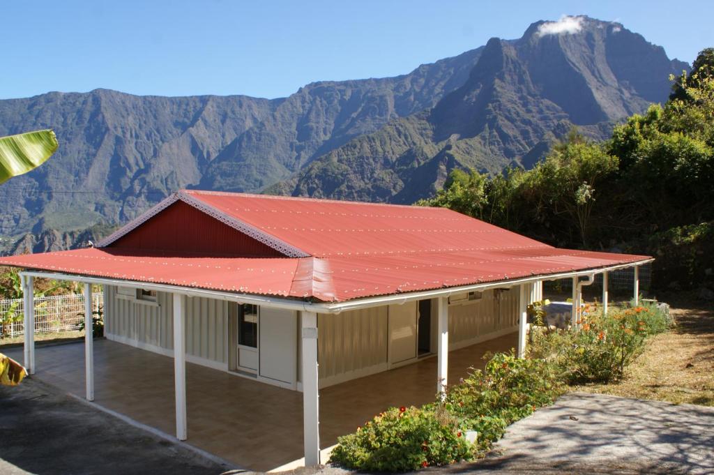 a house with a red roof with mountains in the background at Le Chalet à Joel in Cilaos