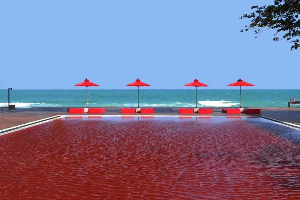 uma piscina com cadeiras vermelhas e guarda-sóis na praia em The Library - SHA Extra Plus em Chaweng
