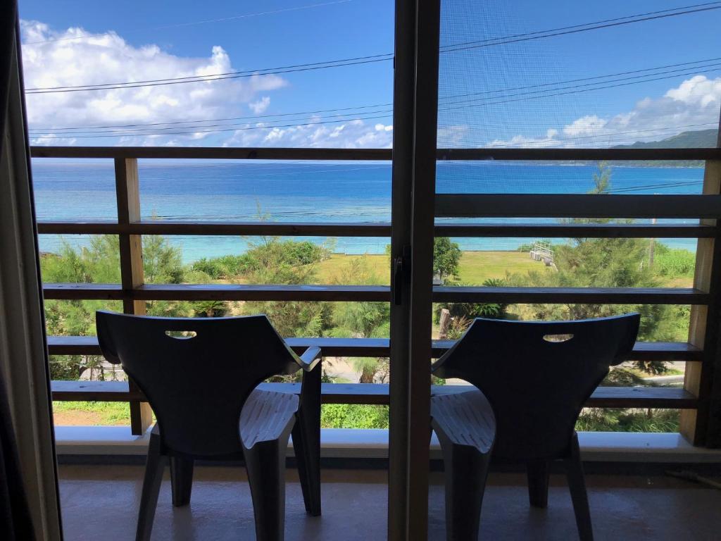 two chairs in front of a window looking out at the ocean at Guest room Halemakana in Amami