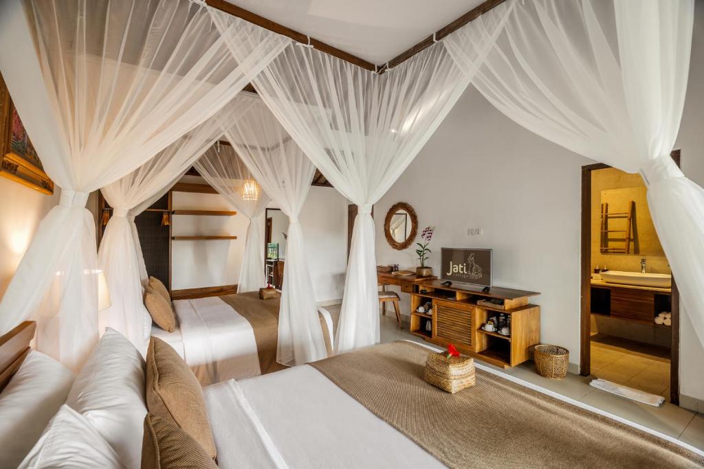 a bedroom with two beds with white drapes at Jati Cottage in Ubud