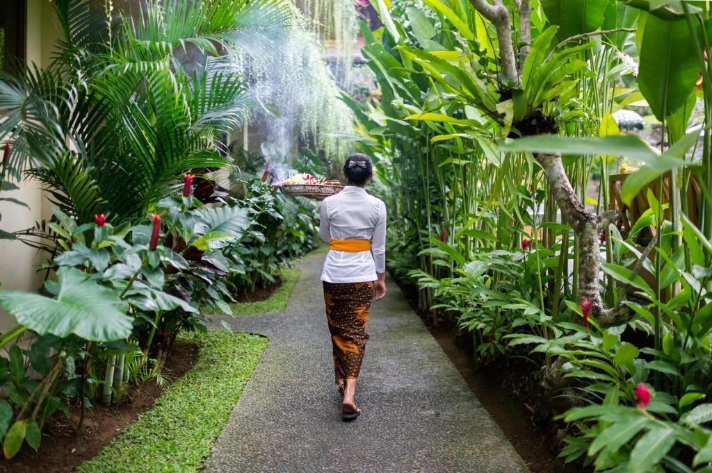 a woman walking down a path through a garden at Jati Cottage in Ubud