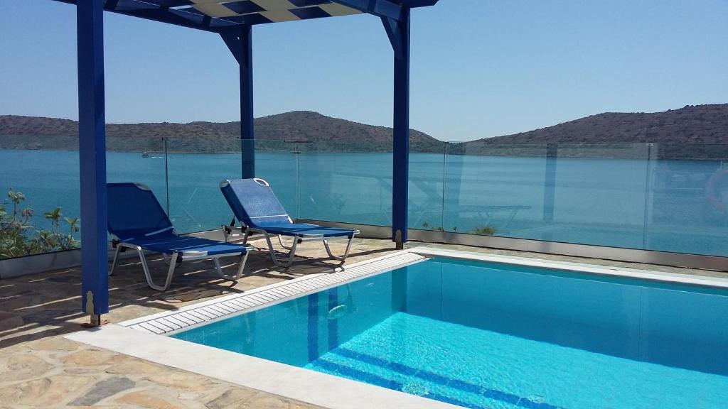 two chairs and a swimming pool with a view of the water at Kavos Bay Apartments Elounda in Elounda