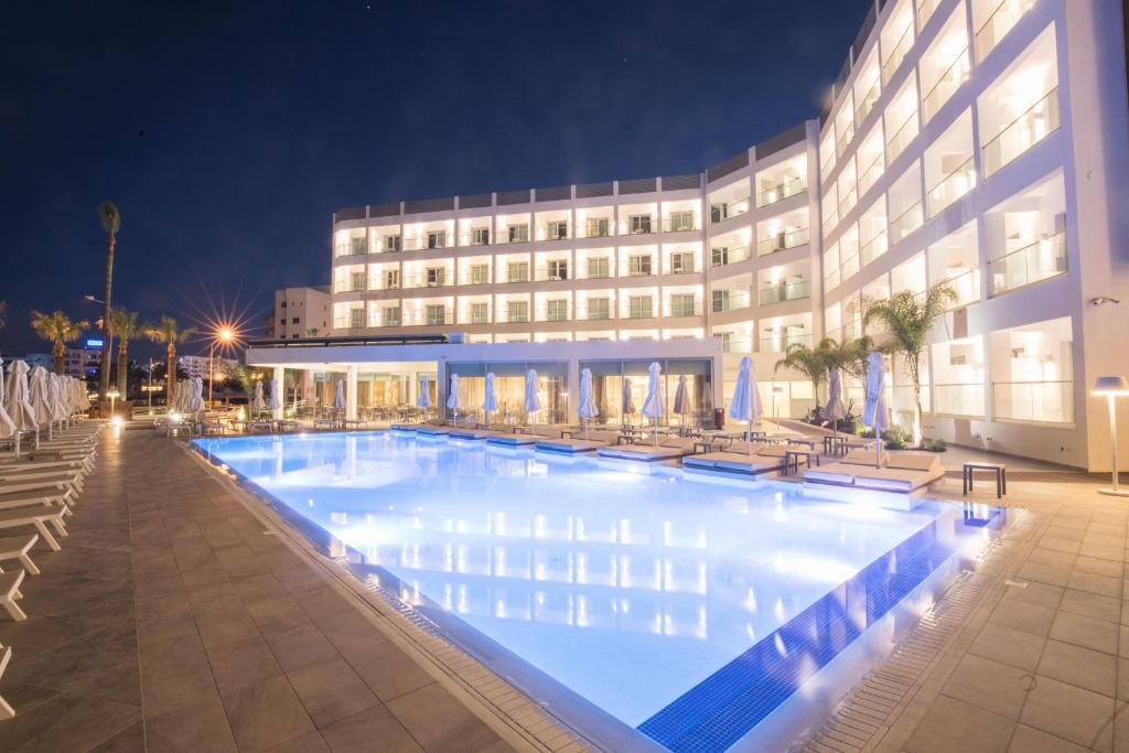 a large swimming pool in front of a building at night at Evalena Beach Hotel in Protaras
