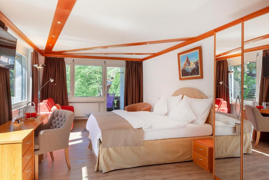 a bedroom with a bed and a desk and chairs at Hotel Beau Rivage in Zermatt
