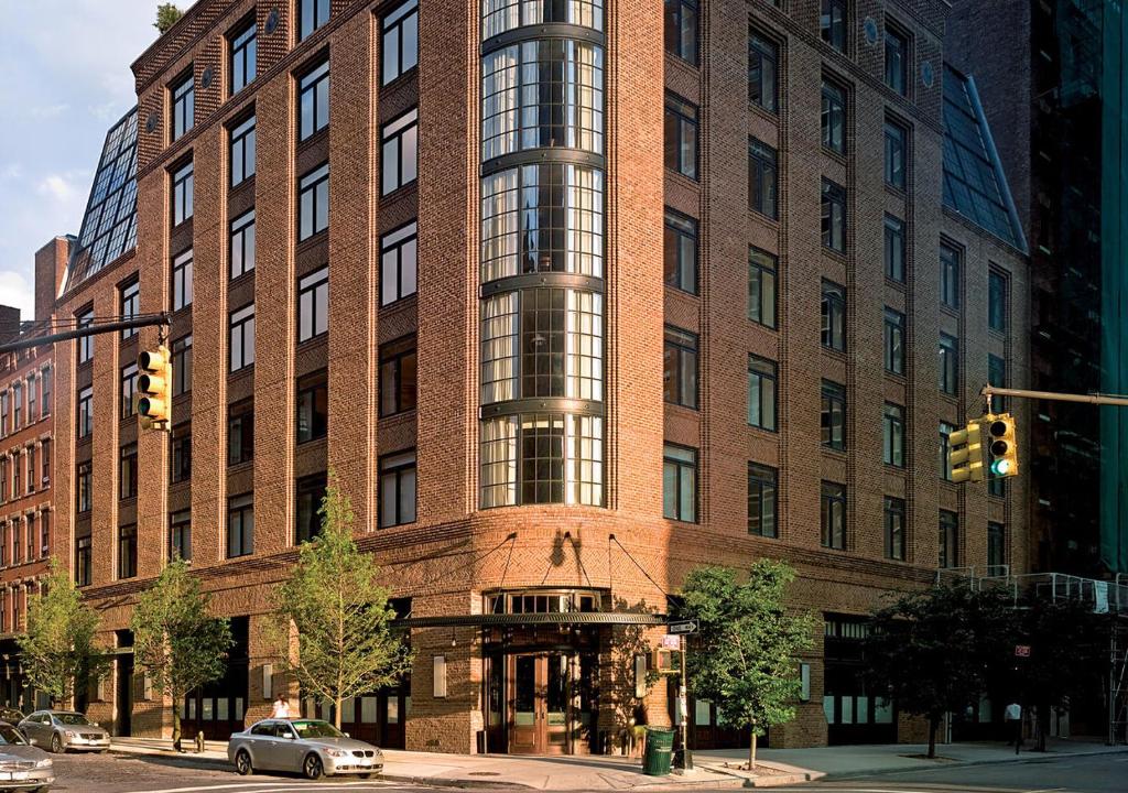 een groot bakstenen gebouw met een auto ervoor geparkeerd bij The Greenwich Hotel in New York