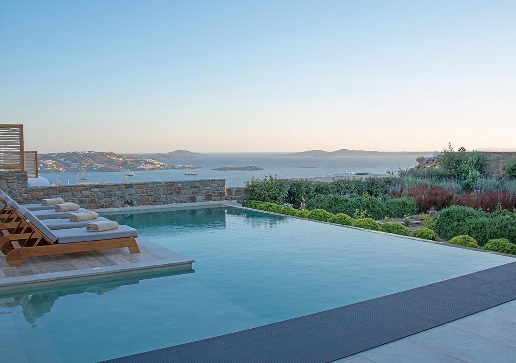 a swimming pool with two lounge chairs and the ocean at M - Mykonos Villas in Tourlos