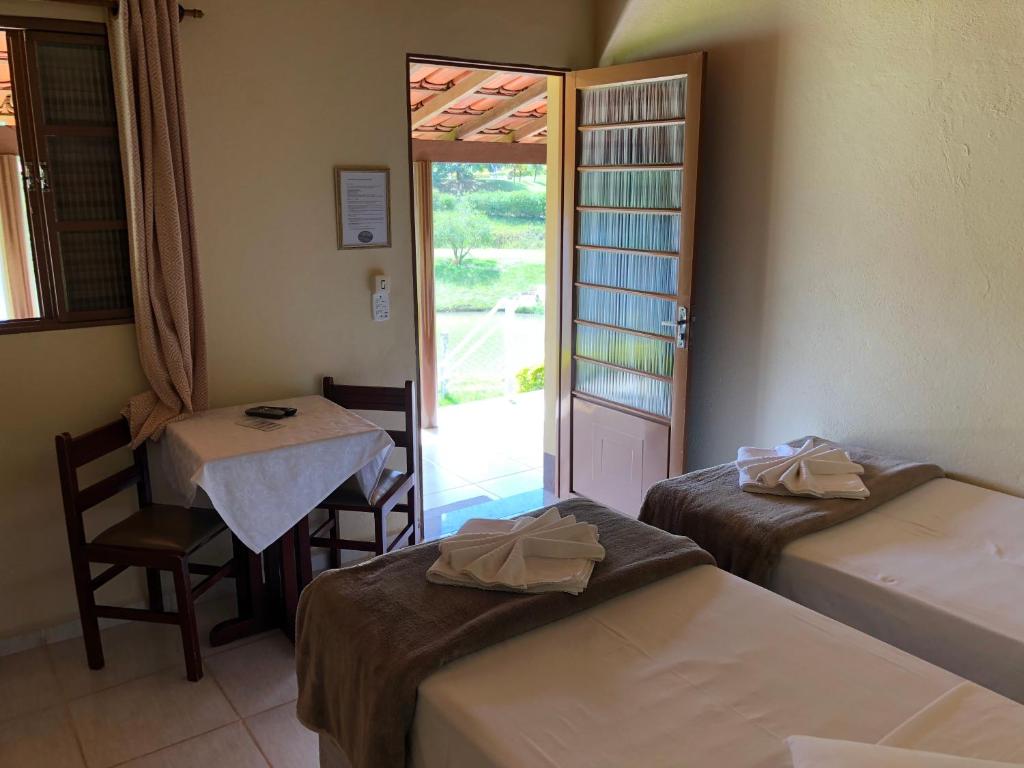 a room with two beds, a table and a window at Hotel Fazenda Santa Maria in Serra Negra