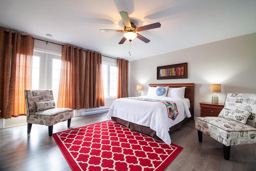 a bedroom with a bed and two chairs and a ceiling fan at Alphabet Fleet Inn in Twillingate