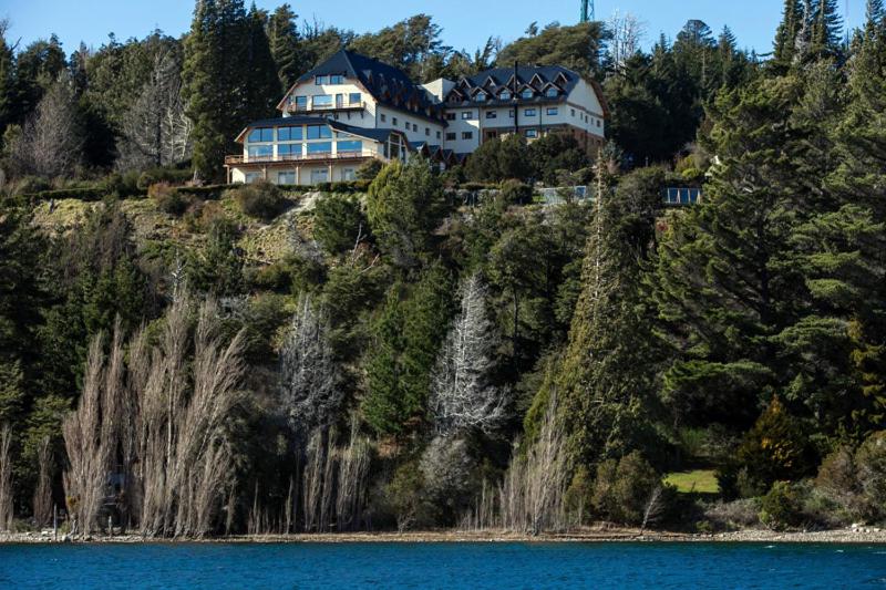 duży dom na szczycie wzgórza obok wody w obiekcie Hotel Amancay w mieście Bariloche