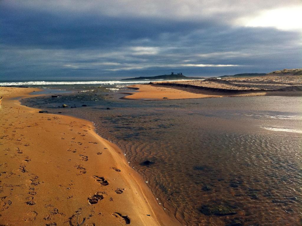 a beach with footprints in the sand and the ocean at The Dunstanburgh Castle Hotel in Embleton