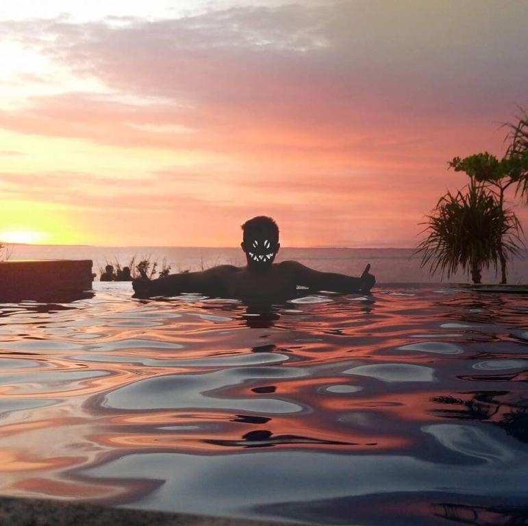 une personne flottant dans un corps d'eau au coucher du soleil dans l'établissement Dodol Lembongan Cliff Sunset, à Nusa Lembongan