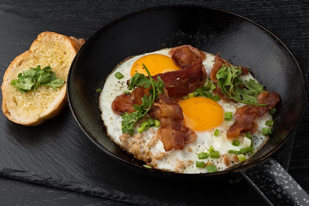 A skillet breakfast of fried eggs, bacon, greens, and toast.