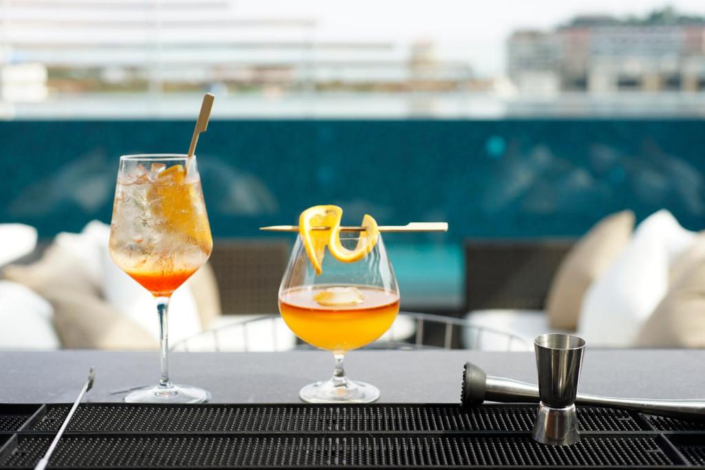Two cocktails are staged at a poolside bar with the pool behind them.