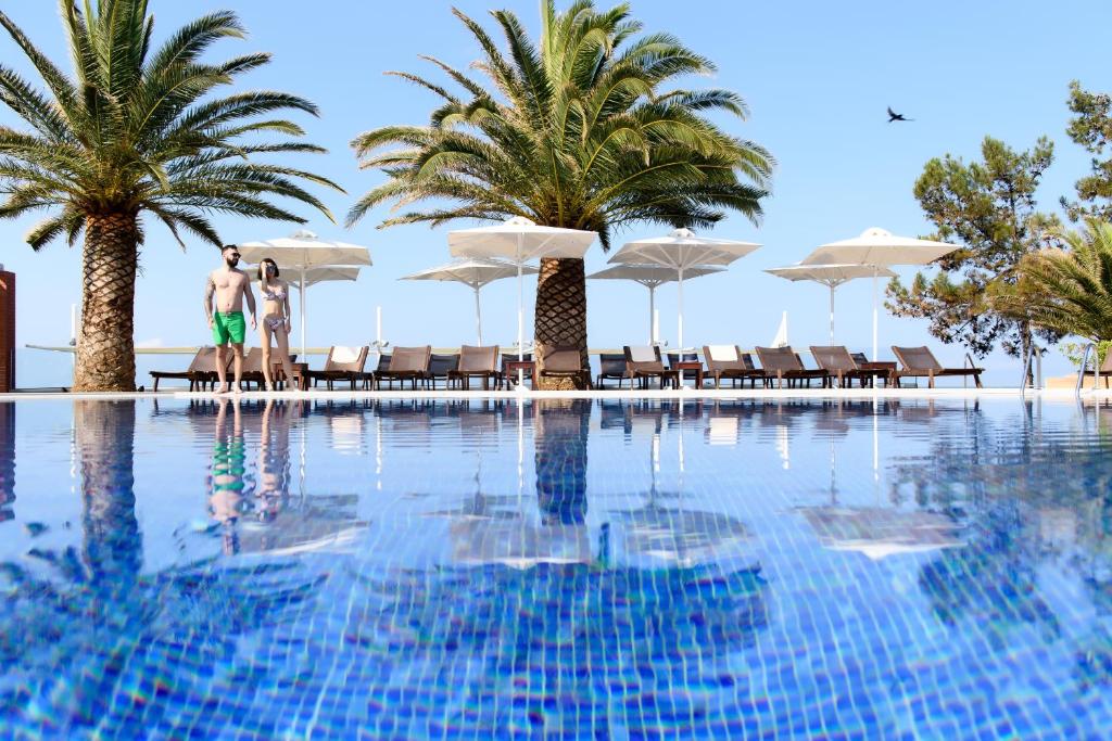 zwei Personen stehen neben einem Pool mit Palmen in der Unterkunft Alexandra Beach Spa Resort in Potos