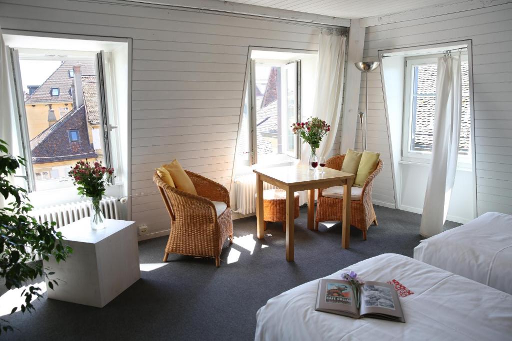 um quarto com duas camas, uma mesa e janelas em Le Café-Hôtel de L'Aubier em Neuchâtel