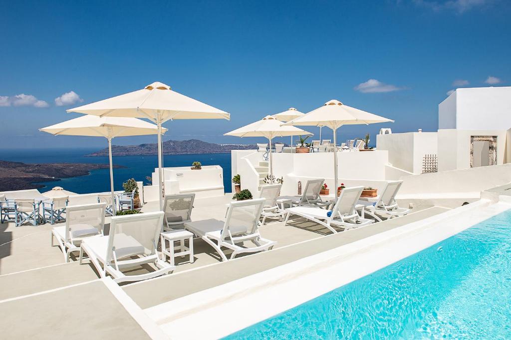 - une piscine avec des chaises et des parasols blancs et l'océan dans l'établissement Pantelia Suites, à Fira