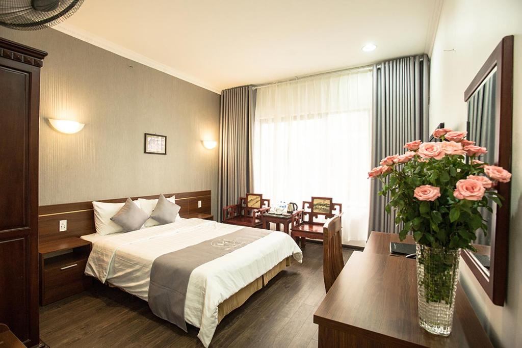 a hotel room with a bed and a vase of pink roses at My Lan Hanoi Hotel in Hanoi