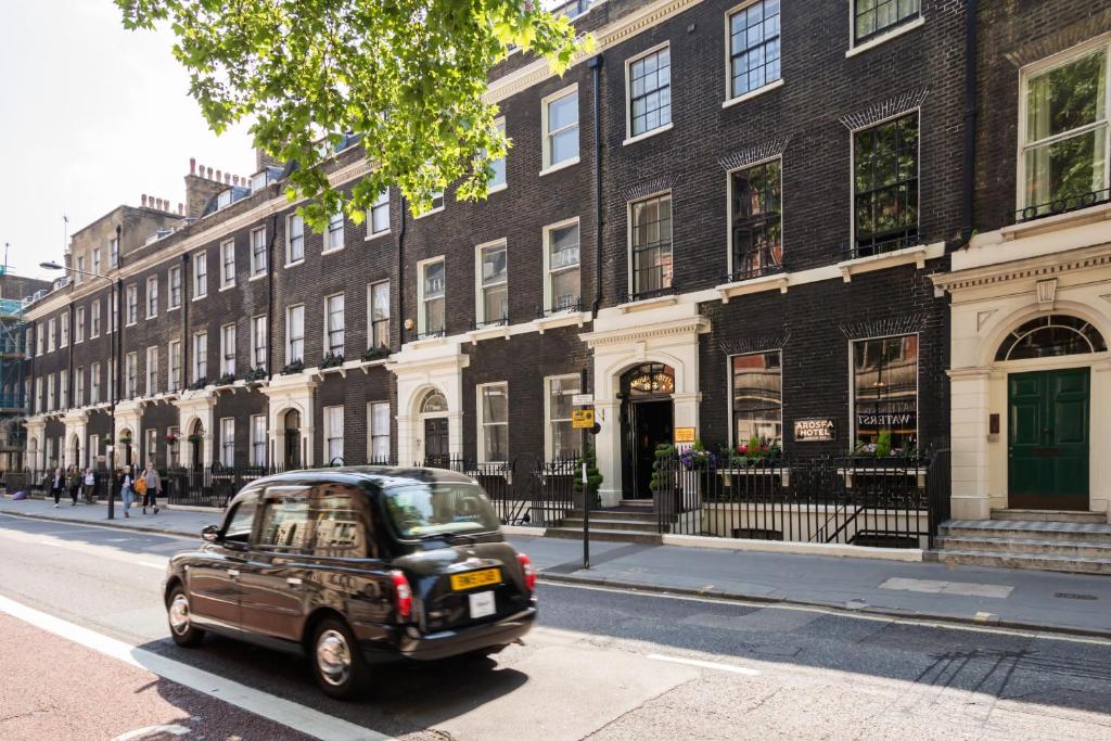 Une petite voiture descend dans une rue en face d'un bâtiment dans l'établissement Arosfa Hotel London by Compass Hospitality, à Londres